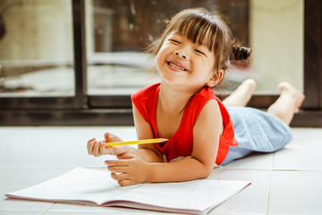 Little girl drawing with colorful crayons and smiling, in colorful room.