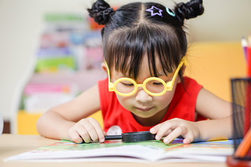 Little girl sitting in the room using a magnifying glass search document, education concept