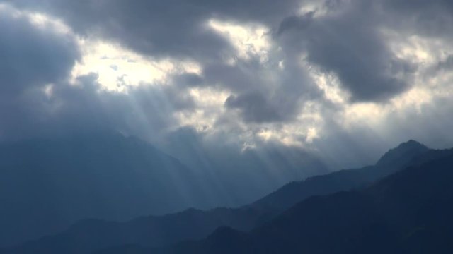 Timelapse of sunlight shining between flowing clouds over mountains