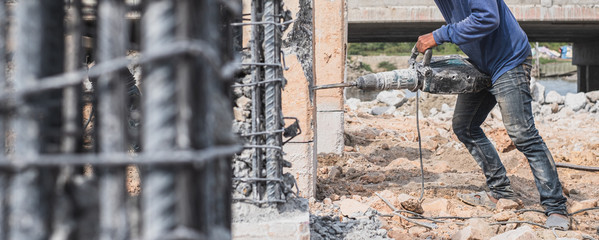 Construction worker holding and using pneumatic jackhammer drill equipment to break reinforced...