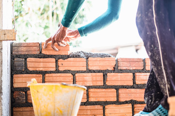 Close up of bricklayer worker's hand installing red brick with trowel putty knife for new house building at construction site.