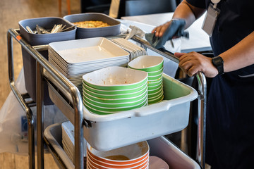 Cleaner staff collecting dirty dishes and put them onto cart in restaurant. © phoderstock