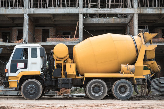 Old yellow cement mixer truck in front of building under construction. Construction machinery.