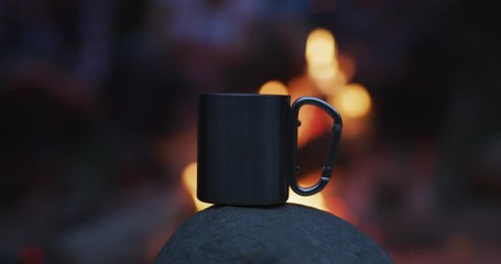 A group of happy young friends relaxing and enjoying summer evening around campfire on the river bank