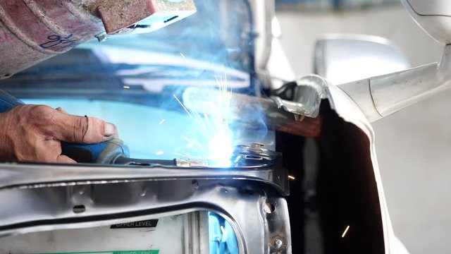 Welding steel with electricity in auto body repair shop, closeup, 4k slow motion