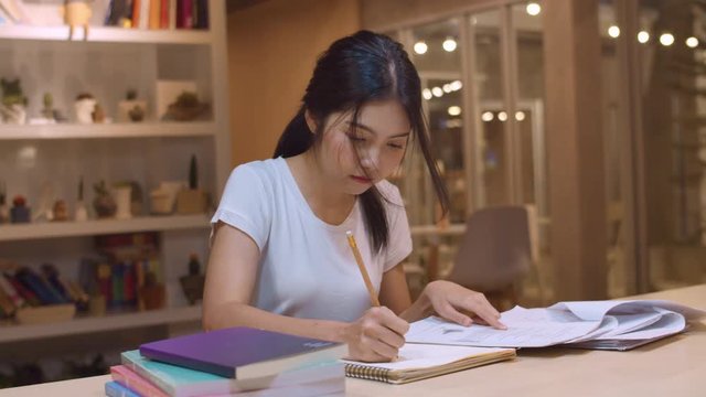 Asian student women reading books in library at university. Young undergraduate girl do homework, read textbook, study hard for knowledge on lecture desk at college campus overtime night. Slow motion.