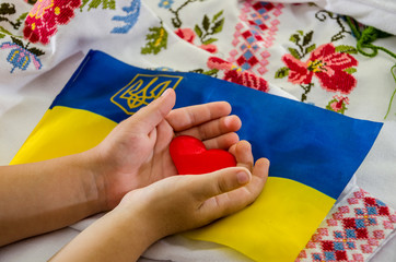 red heart in children's hands on the background of the Ukrainian flag and embroidered shirt
