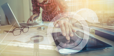 Engineer working  and tablet, laptop with on on architectural project at construction site at desk in office. 