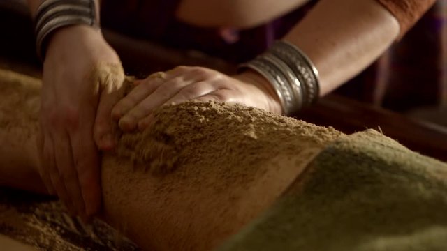 woman is massaging hips of female client by herbal powder, scrubbing and anti cellulite procedure
