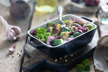 Baked, fried or grilled vegetables in ceramic form on a wooden mtole. Brussels sprouts, onions, garlic, olive oil