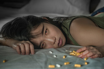 Obraz na płótnie Canvas young beautiful desperate and wasted addict Asian Japanese woman taking drug overdose lying on bed feeling sick and depressed suffering depression breakdown