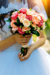Stylish bride in a white dress holds an unusual wedding bouquet close-up. Delicate wedding bouquet of different flowers in the hands of the bride, selective focus.