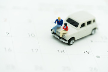 Miniature people sitting on car with calendar.