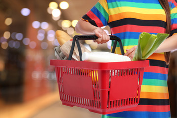 Fototapeta premium Young woman with shopping basket full of different products in supermarket, closeup. Space for text