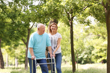 Caretaker helping elderly man with walking frame outdoors