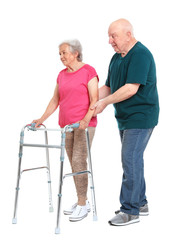 Elderly man helping his wife with walking frame on white background