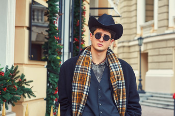 Portrait of a young man in the autumn city . Stylish man in coat and hat on city street
