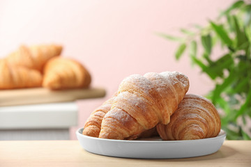 Plate of fresh croissants sprinkled with powdered sugar on table indoors, space for text. French pastry