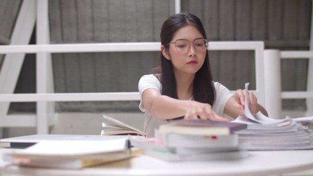 Asian student women reading books in library at university. Young undergraduate girl do homework, read textbook, study hard for knowledge and education on lecture desk at college campus concept.