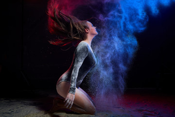 Young teen girl in a dark room during a photoshoot with flour with a colored light and a black background