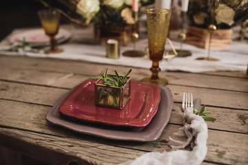 Romantic dinner of the bride and groom on a wooden table with burgundy plates and fresh flowers. 