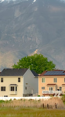 Vertical frame Multi storey homes with white fences against towering mountain and cloudy sky