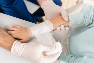 Doctor in blue uniform make elastic bandaged around a boy hand with trauma in his arm.