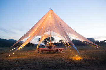 Boho wedding tent in the open air for the bride and groom with decorations, flowers, lights.