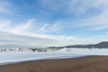 Fototapeta na wymiar Sandy seashore and white waves under sky