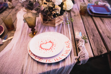 Romantic dinner of the bride and groom on a wooden table with plates and fresh flowers. 
