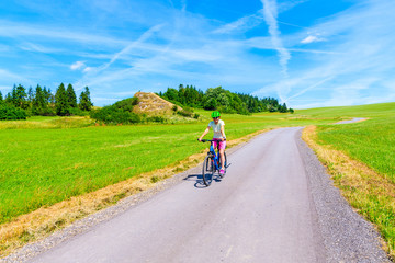 Obraz premium Young woman riding bike on cycling way around Tatra Mountains on sunny summer day, Poland