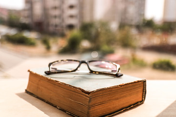 Eye glasses on the old shabby book and blurred background outside the window. Educational concept.