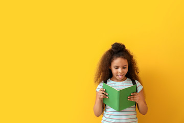 African-American girl reading book on color background