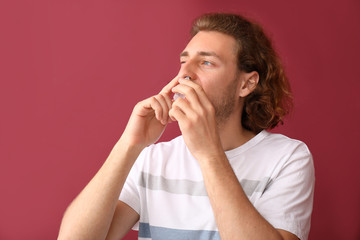 Young man with nasal drops on color background