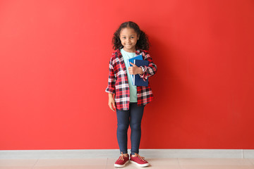 Portrait of adorable little African-American girl with books near color wall