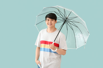 Handsome Asian man with umbrella on color background