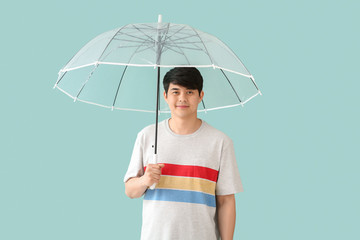 Handsome Asian man with umbrella on color background