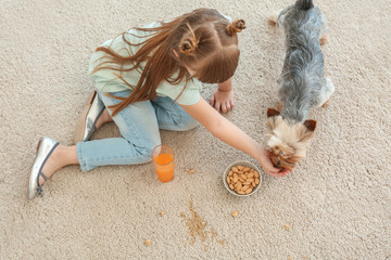 Careless little girl with dog eating nuts and drinking juice while sitting on carpet