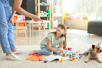Mother scolding little girl for carpet messing up with paints