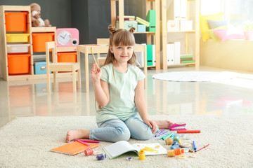 Cute little girl painting while sitting on carpet