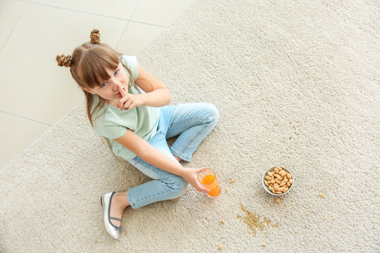 Careless Little Girl Eating Nuts And Drinking Juice While Sitting On Carpet