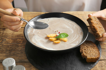 Woman eating tasty cream soup at table, closeup