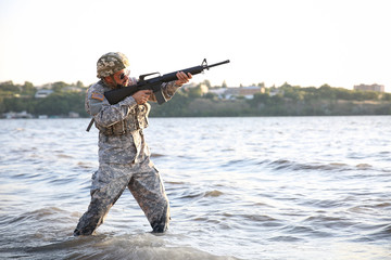 Soldier in camouflage taking aim in river