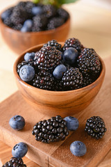 Bowl with tasty blackberries and blueberries on wooden board