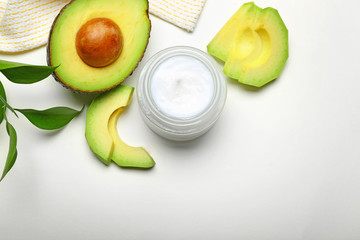 Jar of body cream and avocado on white background
