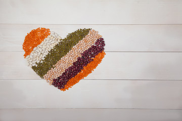 beans, lentils and beans laid out in the form of a heart on a white wooden background with a copy spaes, top view. The concept of healthy nutrition.