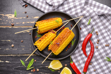 Plate with tasty grilled corn cobs on table