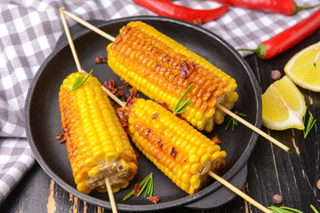 Plate with tasty grilled corn cobs on table