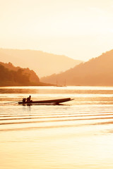 Naklejka na ściany i meble Male fisherman steering wooden fishing boat on the lake at dusk.