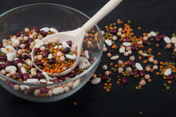 Beans, lentils, mung bean and peas in a glass bowl and wooden spoon on a black background. Concept - Keto Diet